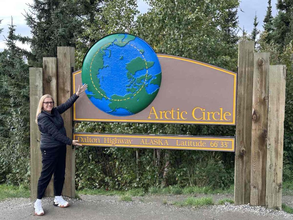 Traveller standing by the iconic Arctic Circle sign on the Dalton Highway, marking latitude 66°33′.
