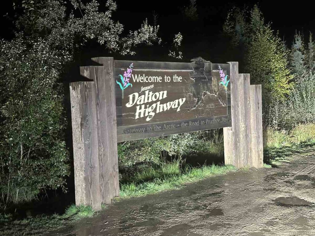 Wooden roadside sign at night welcoming travellers to the James Dalton Highway, gateway to the Arctic.