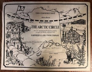 A certificate from the Northern Alaska Tour Company awarded to Helen Hatzis for crossing the Arctic Circle on September 4, 2025, decorated with illustrated Alaskan wilderness scenes.