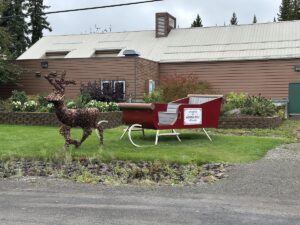 Decorative sleigh and reindeer statue on a green lawn in North Pole, Alaska, with a sign reading “Welcome to North Pole, Alaska.”