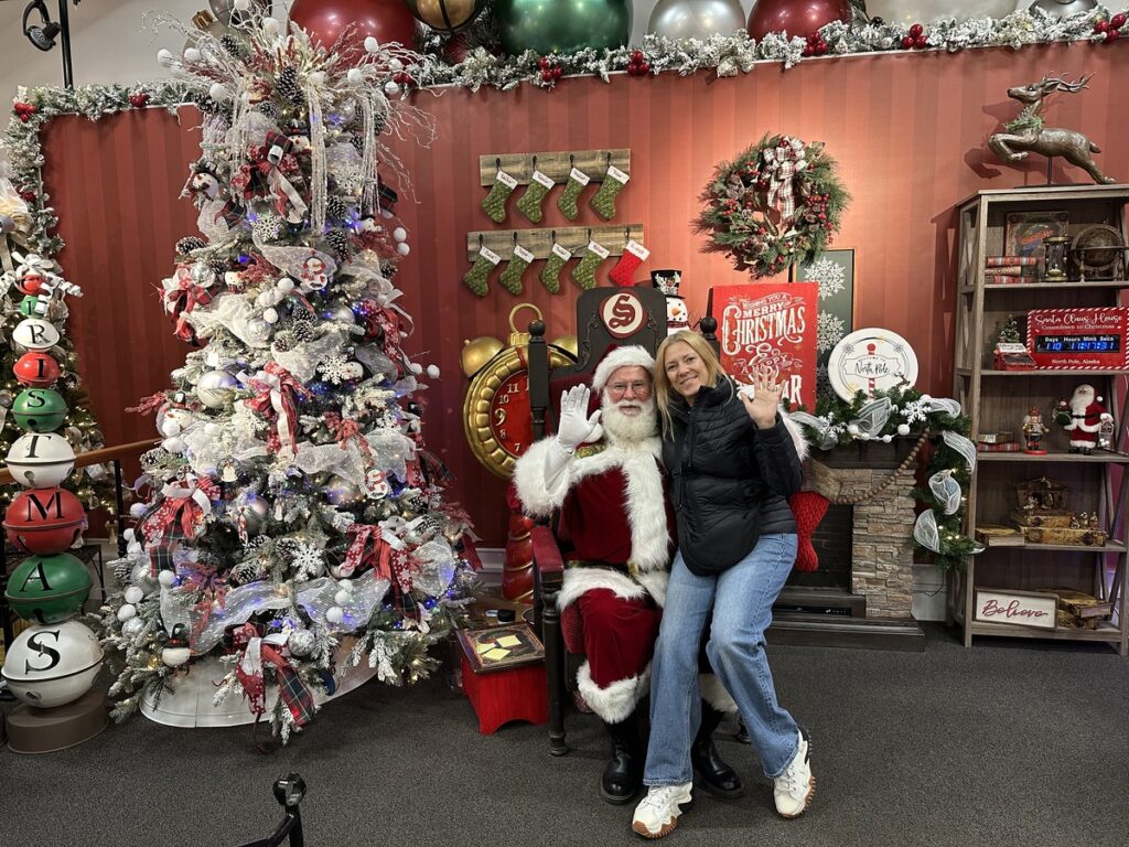 The author is sitting with Santa Claus for a festive photo inside the Santa Claus House in North Pole, Alaska.