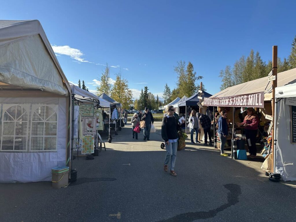 Row of vendor tents with shoppers strolling a wide central aisle beneath blue sky.