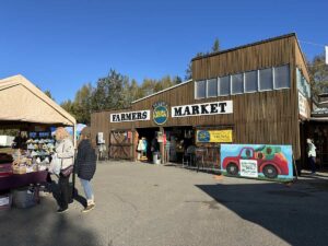 Wooden market building with “Farmers Market” sign and Alaska Grown logos on a sunny day.