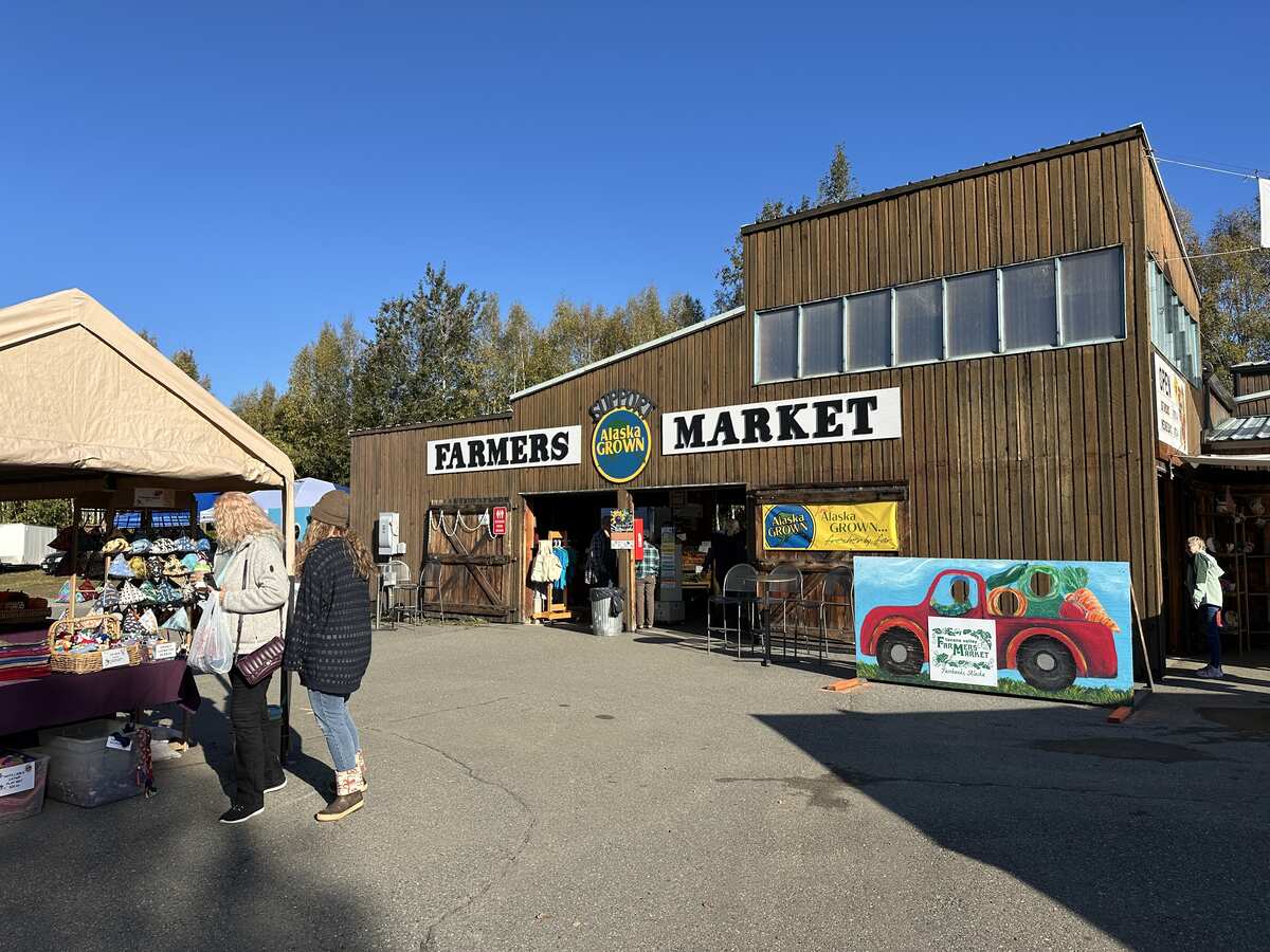 Wooden market building with “Farmers Market” sign and Alaska Grown logos on a sunny day.
