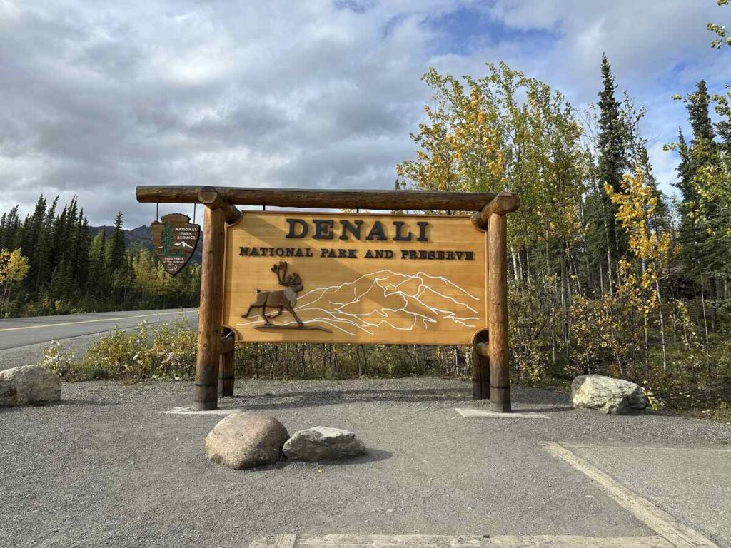 Wooden “Denali National Park and Preserve” entrance sign framed by autumn birch and dark spruce.