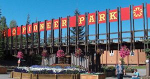 Entrance sign at Pioneer Park in Fairbanks, Alaska, with bold red-and-gold lettering and hanging flower baskets, marking the gateway to the historic theme park.