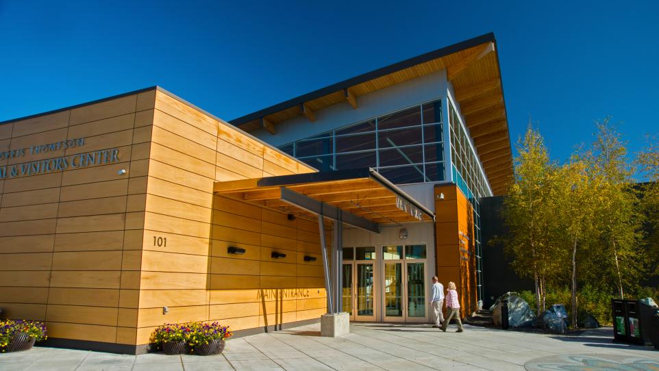 Exterior of the Morris Thompson Cultural and Visitors Center in Fairbanks on a clear day, with visitors walking toward the entrance.