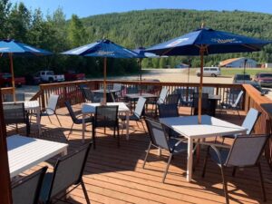 Outdoor deck at the Turtle Club in Fairbanks, Alaska, with tables, chairs, and blue umbrellas set against a backdrop of forested hills.