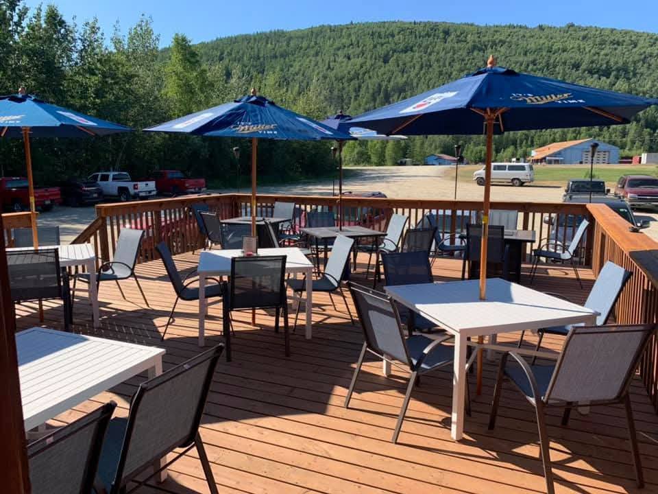 Outdoor deck at the Turtle Club in Fairbanks, Alaska, with tables, chairs, and blue umbrellas set against a backdrop of forested hills.