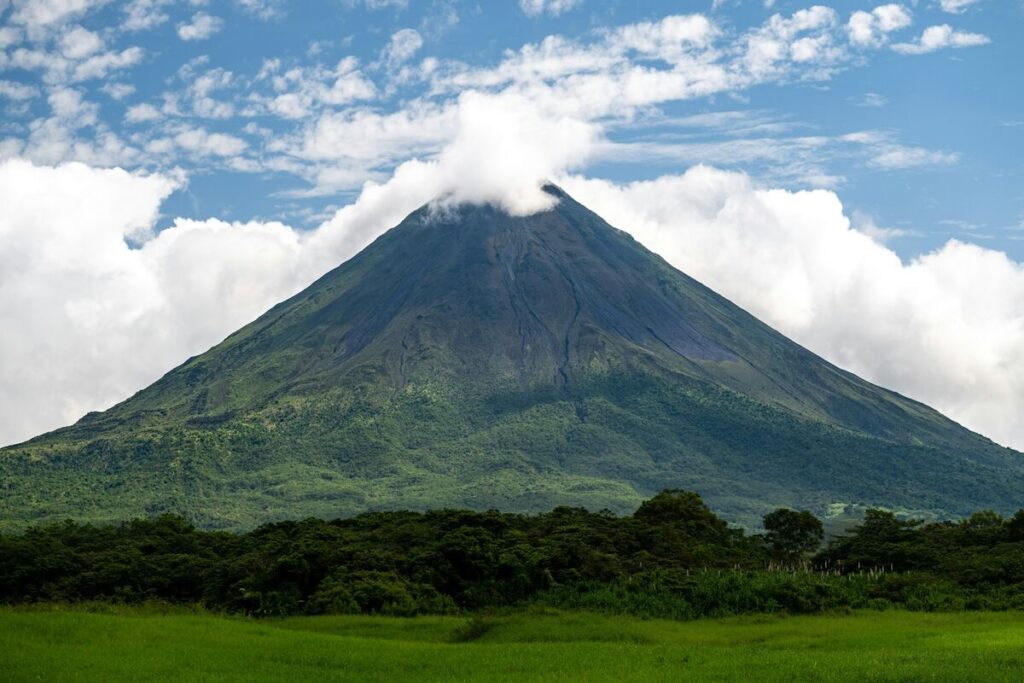 Arenal Volcano rising from green rainforest under a blue-and-white sky in northern Costa Rica.