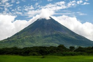 Arenal Volcano rising from green rainforest under a blue-and-white sky in northern Costa Rica.
