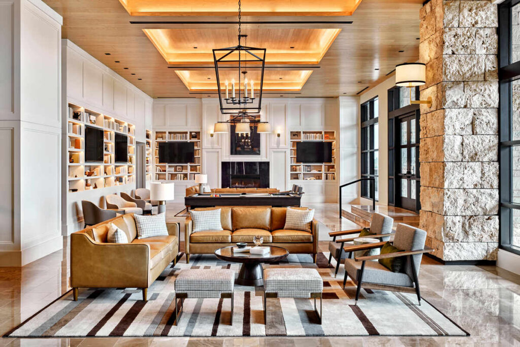 Bright, contemporary lounge with leather sofas, armchairs, a central coffee table, built-in bookcases, and a pool table set beneath warm, recessed ceiling lights.