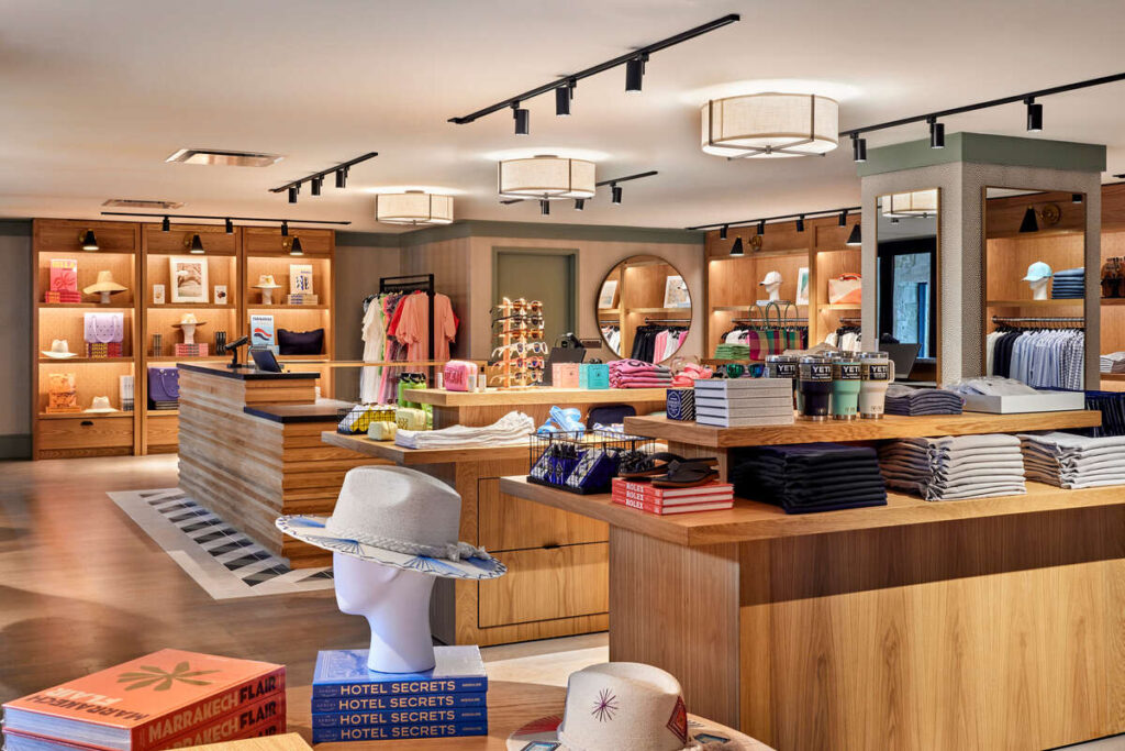 Bright resort boutique with wooden display tables and shelves showcasing hats, books, resort wear, accessories and colourful gifts under soft ceiling lights.