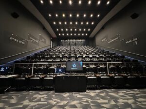 Dark, steeply tiered theatre filled with leather recliner seats facing a large screen, with words like “Work Ethic,” “Commitment,” “Accountability,” and “Passion” etched on the side walls.