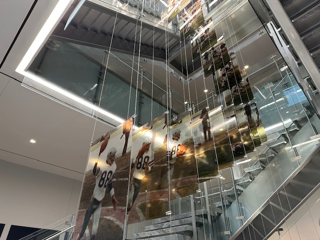 Tall glass stairwell installation with multiple suspended panels showing action shots of a Cowboys receiver wearing number 88, creating a cascading effect of movement.
