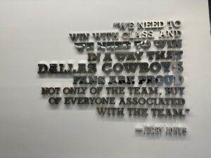 Close-up of a wall installation with raised metallic letters displaying a Jerry Jones quote about winning with class and making fans proud.