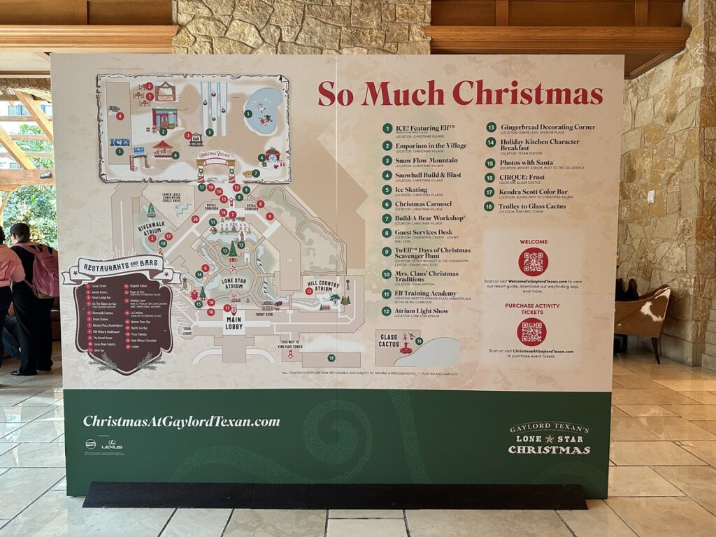 A large “So Much Christmas” sign stands in the Gaylord Texan lobby, showing a detailed map of the resort with numbered holiday attractions, dining options, and QR codes for tickets and information.