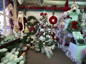 A packed holiday boutique filled with Christmas décor, from a fully decorated tree and wreaths to figurines, ornaments, and a life-sized Santa standing by the window.