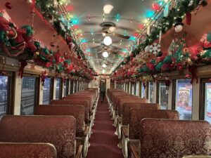 The interior of a vintage railcar dressed head to toe for the season, with red patterned seats, garlands and bows lining the luggage racks, and strings of multicoloured lights running the length of the ceiling down a long central aisle.