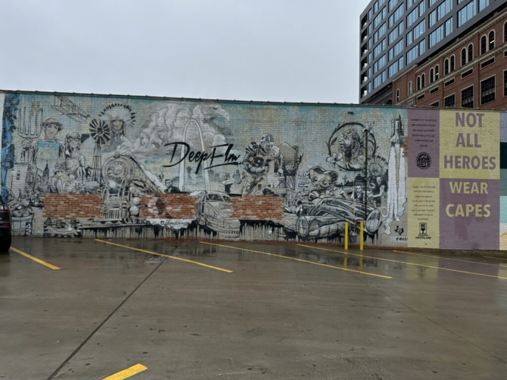 Large monochrome mural on a brick wall in Deep Ellum featuring historic Texas figures and the words “Deep Ellum” and “Not All Heroes Wear Capes.”