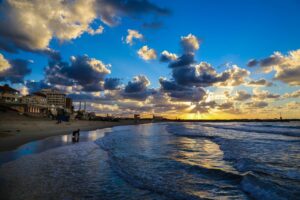 Dramatic sunset over a densely built coastline and rolling waves, capturing the tension between natural beauty and human presence.