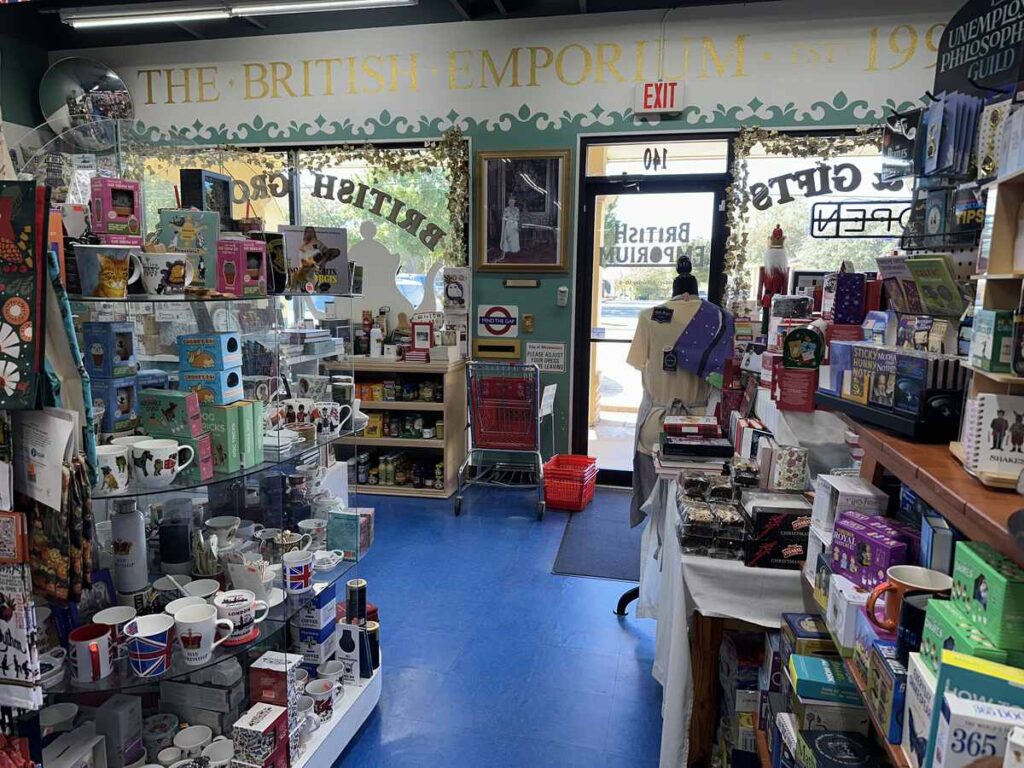 Interior of the British Emporium in Grapevine, Texas, showing shelves filled with British mugs, gifts and groceries, with the front door and “The British Emporium” sign visible in the background.