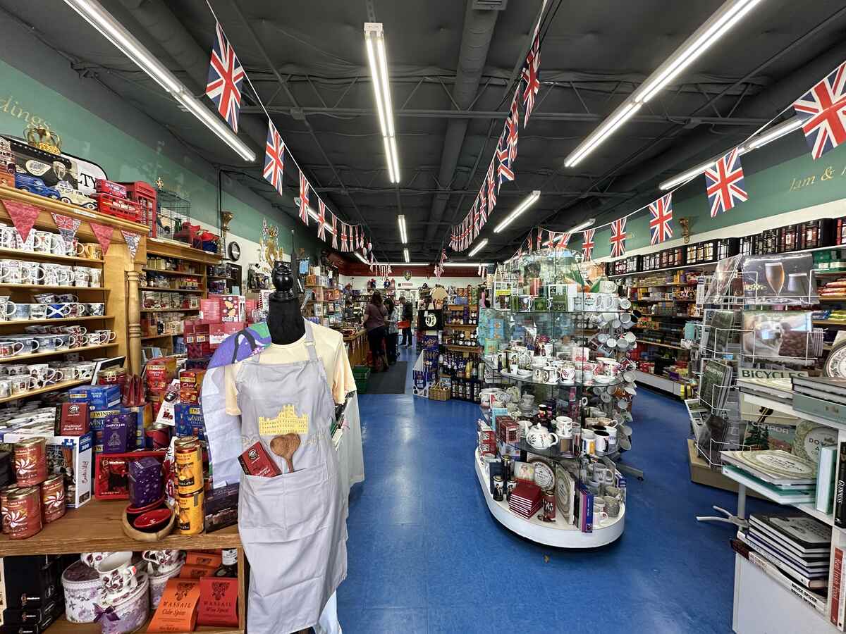 Wide view down the main aisle of the British Emporium, with Union Jack bunting strung across the ceiling and displays of mugs, tins and groceries lining both sides of the shop.