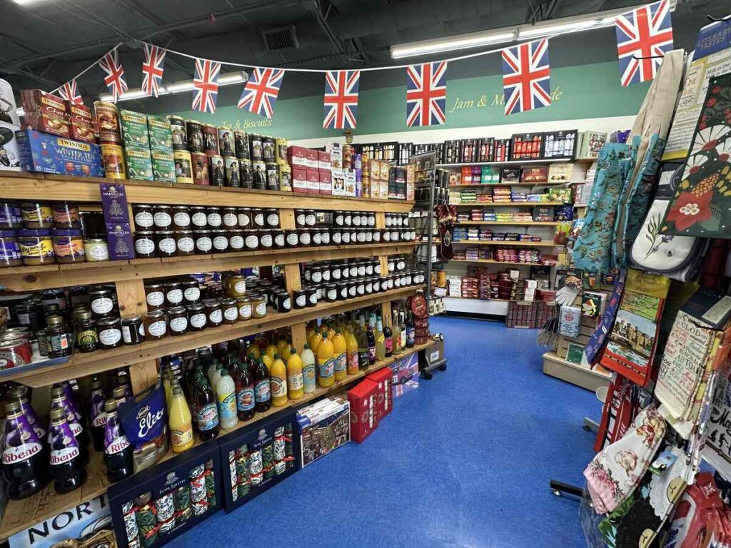 Shelves at the British Emporium lined with jars of jam and marmalade, bottles of cordial and juices, and rows of biscuits and pantry staples beneath a string of Union Jack flags.