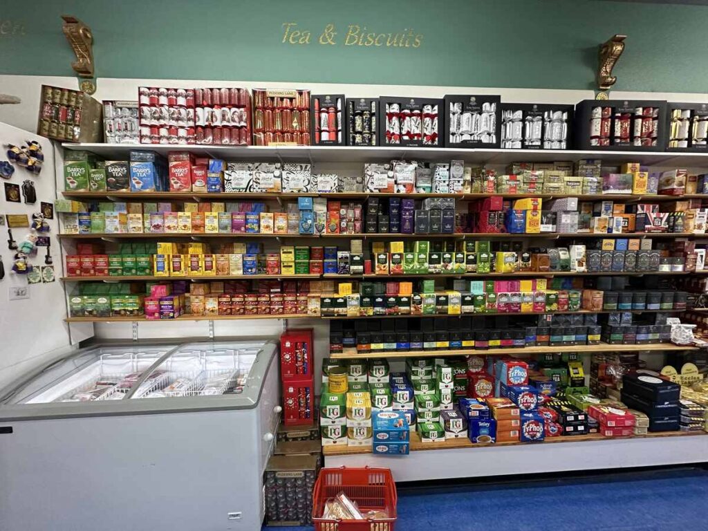 Wall of teas and biscuits at the British Emporium, with rows of boxed teas from various brands stacked above freezers and cases of packaged treats.