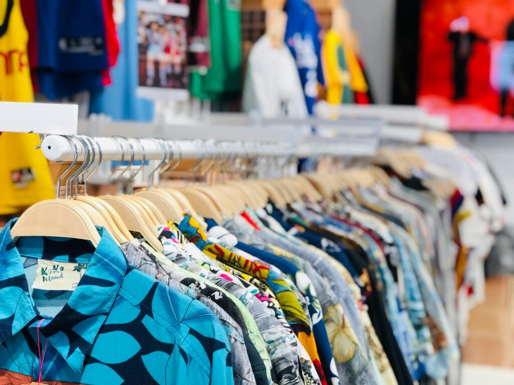 Row of patterned shirts on wooden hangers in a clothing shop, with colourful garments blurred in the background.