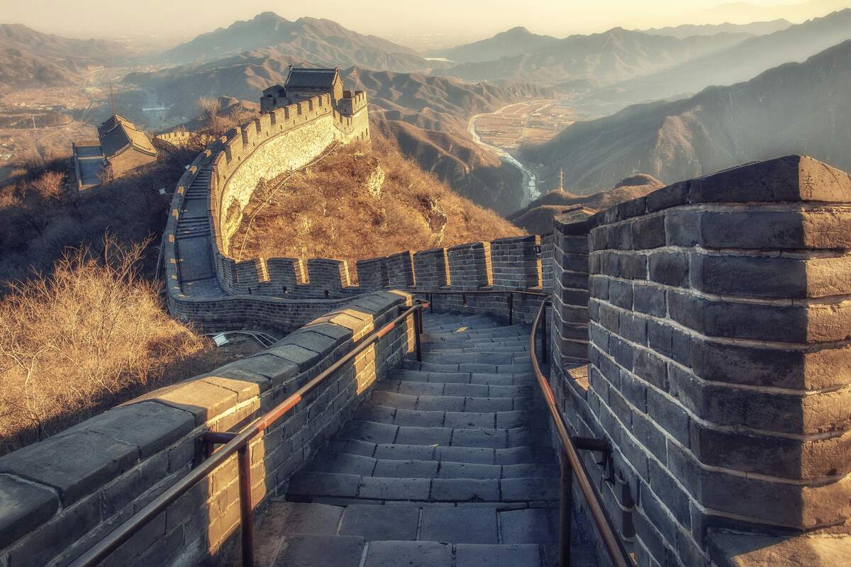 Stone steps along the Great Wall of China overlooking mountainous terrain at sunset.