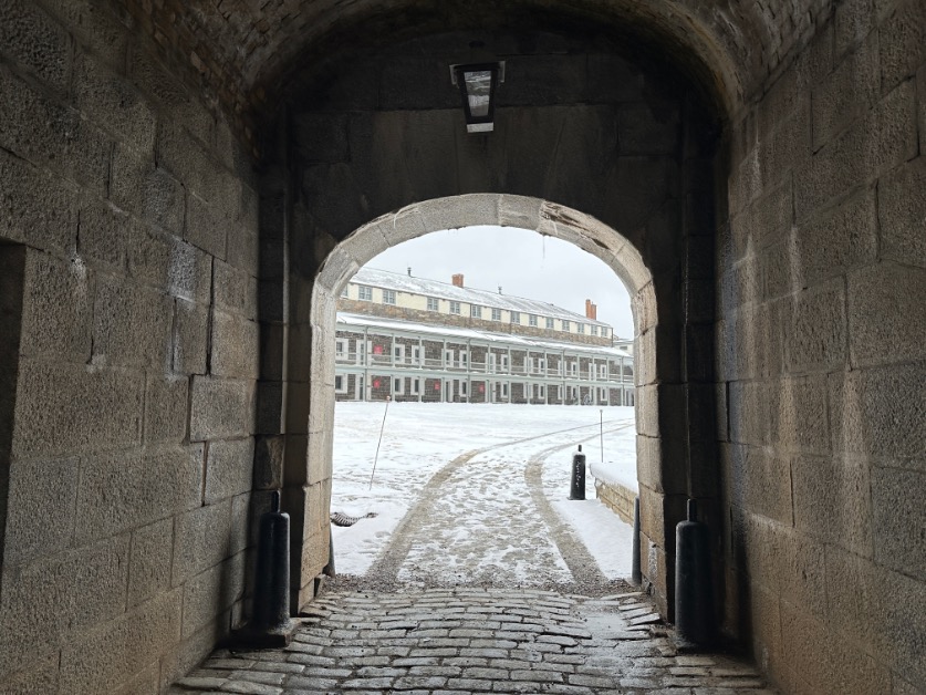 Stone archway at the Halifax Citadel opening onto a snowy courtyard and historic barracks.