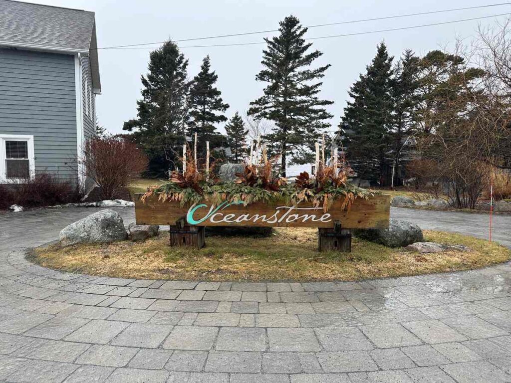 Oceanstone resort sign at the entrance with cottages and trees in the background on a rainy day.
