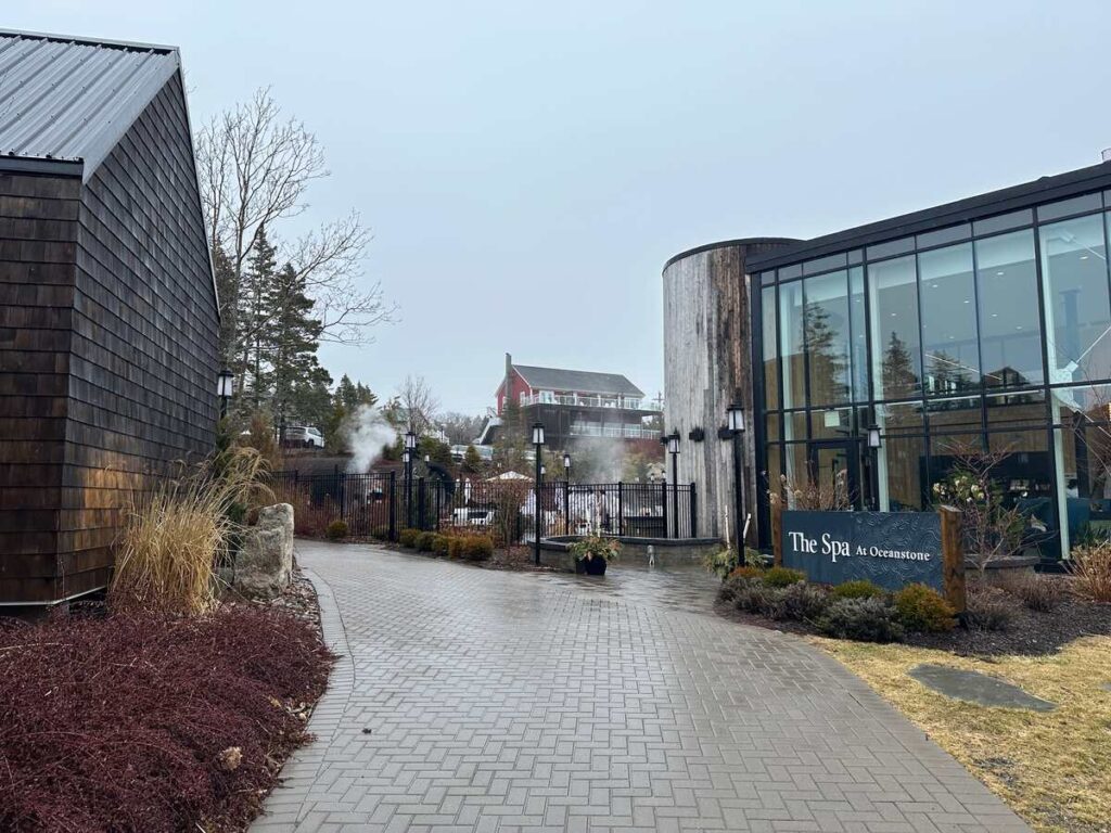 Walkway leading toward The Spa at Oceanstone, with the spa building and steaming outdoor pools visible ahead.