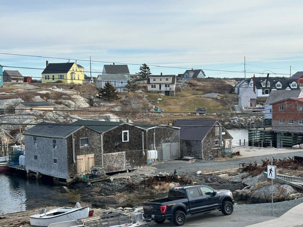 Dark wooden fishing sheds sit beside the harbour in Peggy’s Cove, with homes and granite slopes rising behind them