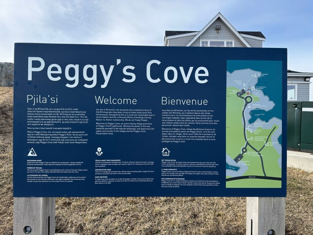 Large welcome sign for Peggy’s Cove with Mi’kmaq, English, and French text beside a map of the village.