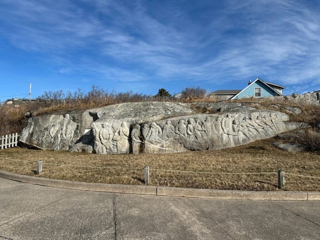 Granite carving by William E. deGarthe is etched into a large rock face in Peggy’s Cove, beneath a bright blue sky.