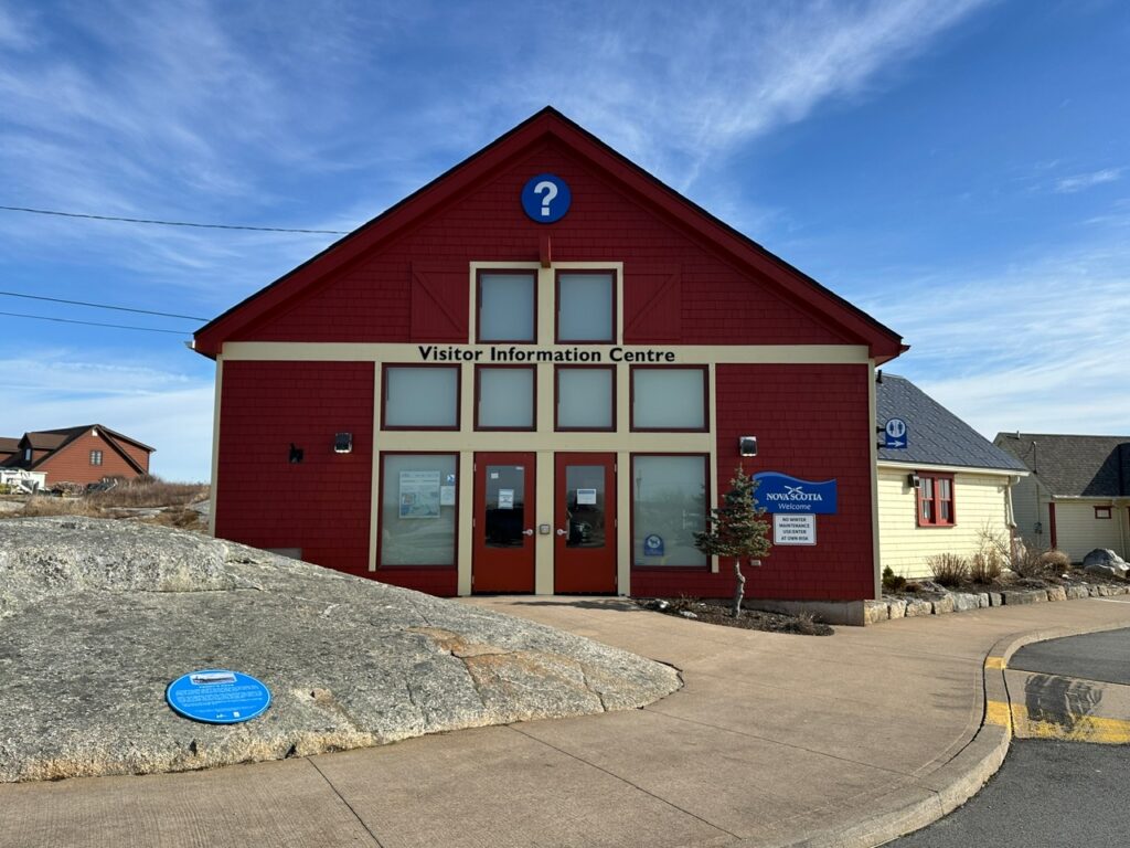 Red visitor information centre building in Peggy’s Cove with white trim and a question mark symbol above the entrance.