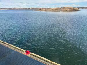 View of Halifax Harbour from Pier 21, with calm blue water in the foreground and Georges Island visible in the distance. Red pier 21 marker.