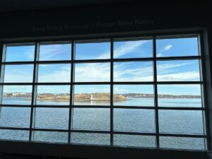 Large grid window inside Pier 21 framing a bright view of Halifax Harbour and Georges Island beyond the glass.