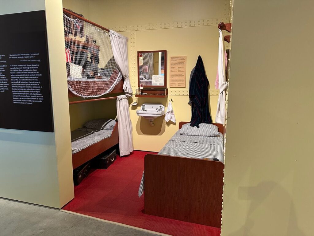 Recreated immigrant cabin exhibit at Pier 21 with bunk beds, a narrow single bed, a small sink, hanging robes, and compact personal space.