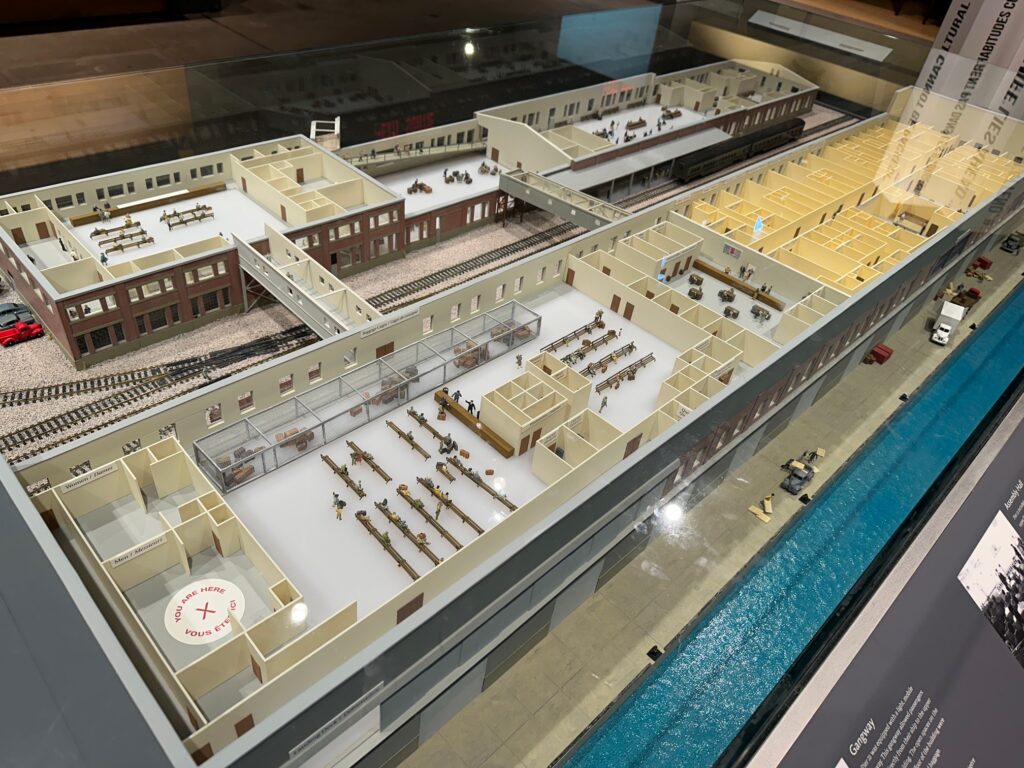 Detailed overhead model of Pier 21 and its annex buildings showing waiting areas, tracks, passageways, rooms, and the adjacent waterway.