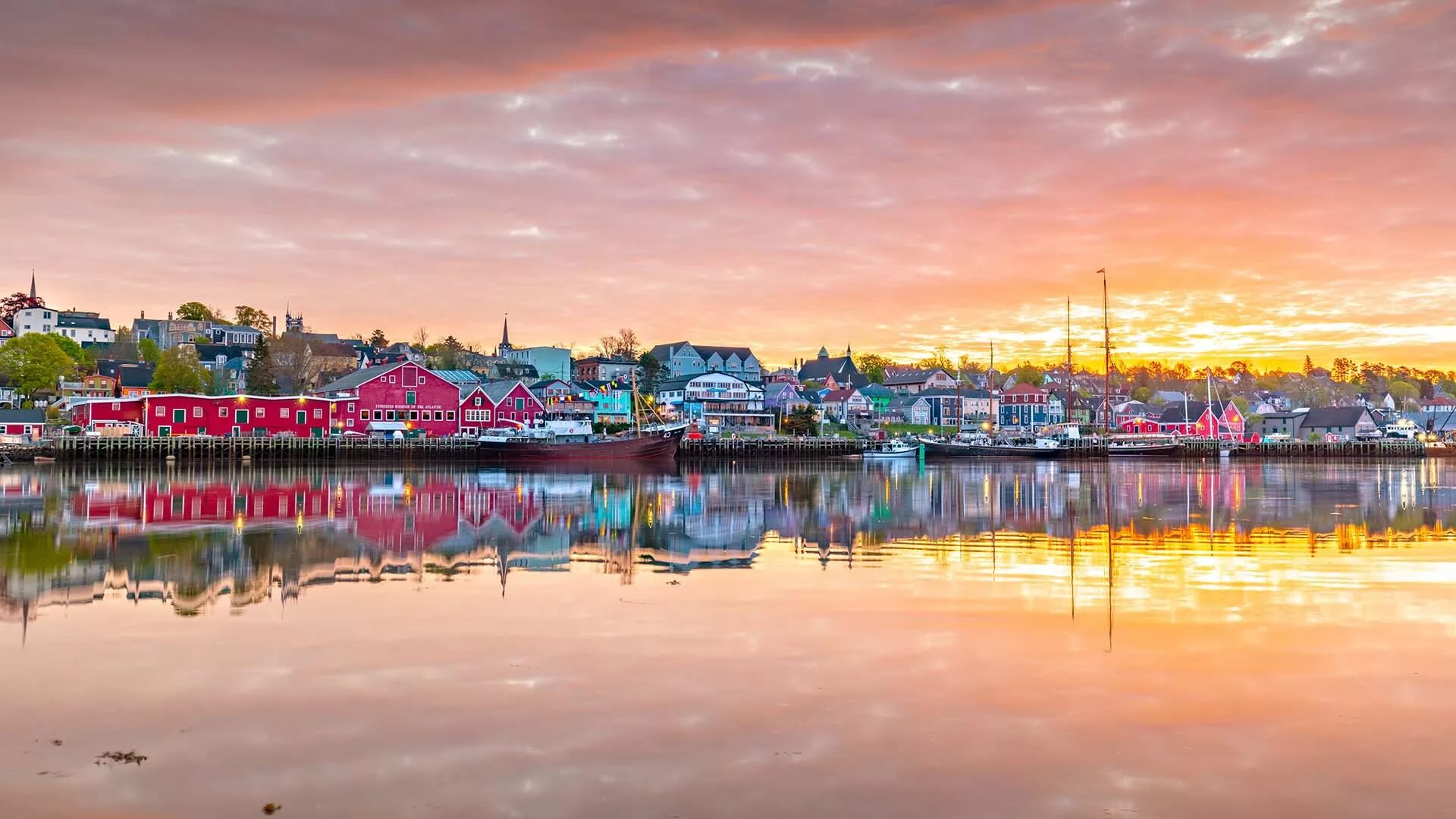 Panoramic view of Lunenburg’s colourful waterfront at sunset, with rows of bright buildings reflected in calm harbour water.