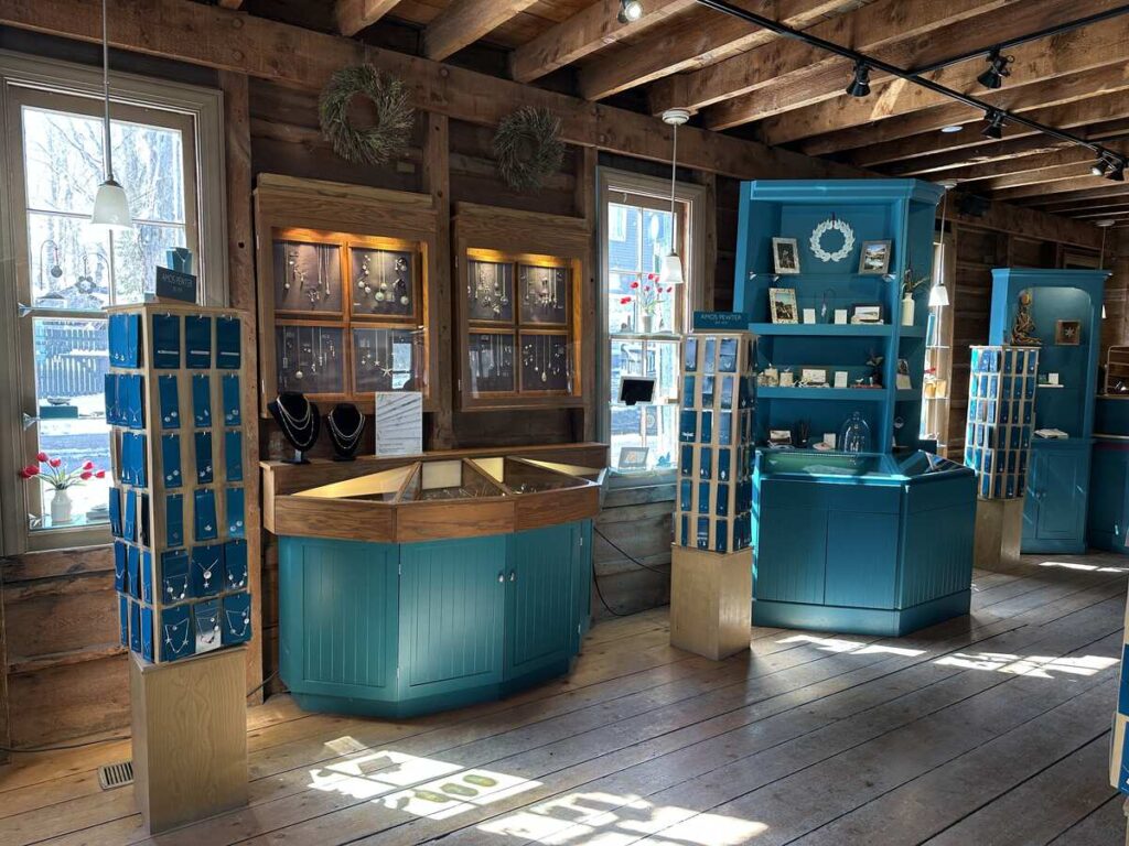 Interior of Amos Pewter’s retail space with wood-beam walls, turquoise display cabinets, jewelry cases, and sunlight streaming across the floor.