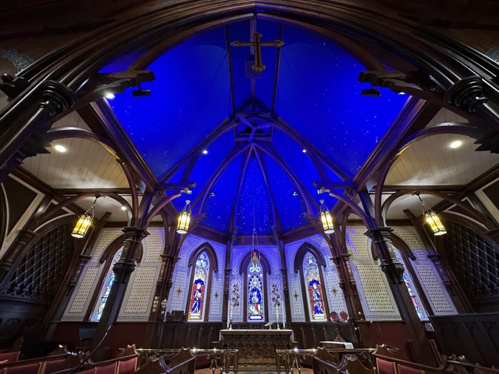 Interior of St. John’s Anglican Church in Lunenburg, showing the altar, stained-glass windows, dark wood arches, and the blue painted ceiling dotted with stars.
