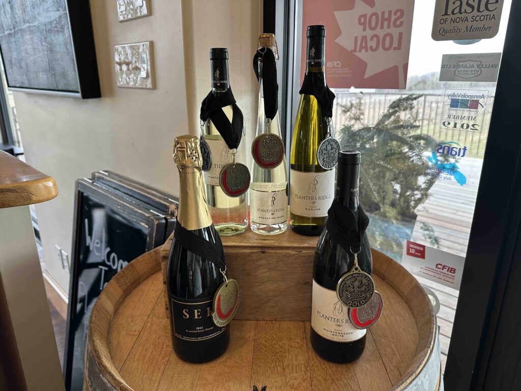 Several bottles of Planters Ridge wine, some decorated with award medals, are displayed on top of a wooden barrel near a window.