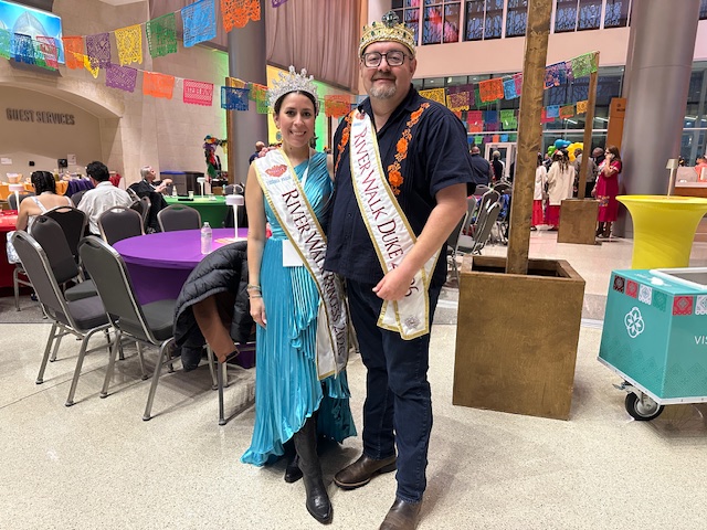 Two Fiesta participants wearing crowns and ceremonial sashes pose together inside the event space during the welcome reception.