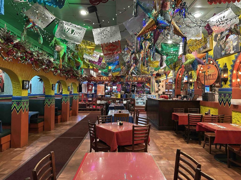 Dining area with bright yellow walls, papel picado banners overhead, and neatly set tables inside Mi Tierra Café