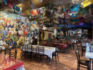 Spacious dining room inside Mi Tierra Café with long tables, colourful papel picado banners, and large murals covering the walls