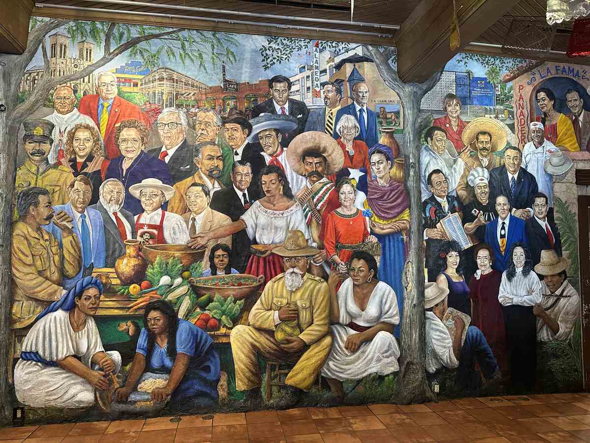 Large colourful mural covering two walls featuring historical figures, artists, and scenes of Mexican-American life